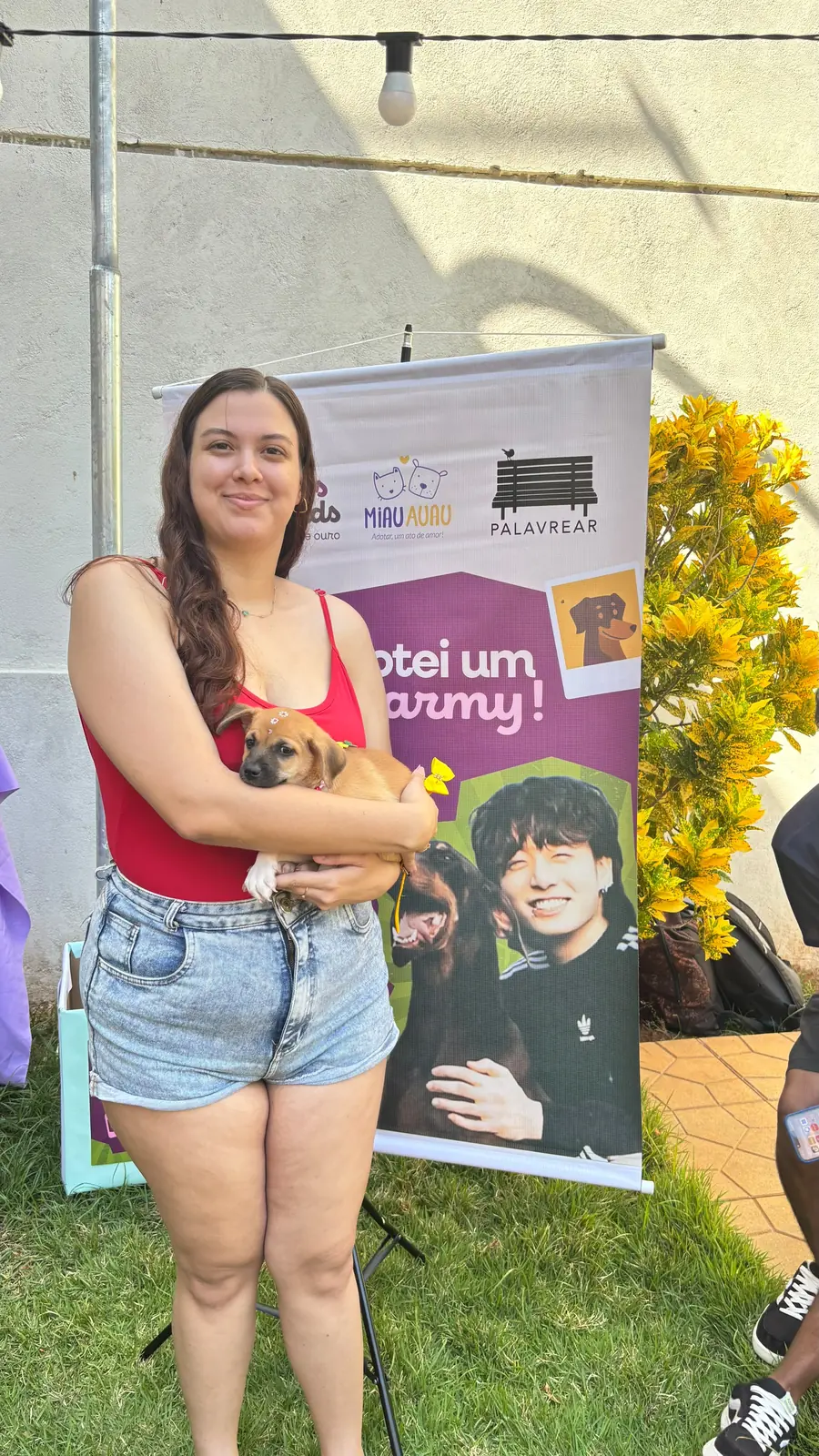 Voluntária do Bam's Friends segura um filhote no colo em frente ao banner do evento de adoção.